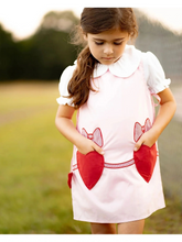 Load image into Gallery viewer, Fully lined light pink jumper features front heart pockets and a single button closure at the back, it’s full of love and charm. Pink ties with red hearts under each arm help adjust the fit perfectly.
Perfectly pairs with a white Peter Pan collar blouse or a cozy turtleneck for sweet white-shirt combos that make dressing up fun and easy.