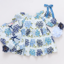 Load image into Gallery viewer, Nice Threads! A patchwork of richly hued blue blossoms are embroidered onto a pure white ground on our Girls Brooke Dress in Blue Quilt Flower Embroidery. Classic design elements include a rounded neck, a three tiered full skirt, ruffle detail at the sleeve and our signature glitter buttons at the back. 