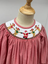 Load image into Gallery viewer, Dress your little one in festive charm with the Girls Rockin' Reindeer Bishop Dress from Cape Point Clothing Co. This vibrant red and white gingham dress features a smocked neckline adorned with playful dancing reindeer and Santa motifs, perfectly capturing holiday joy. The dress style offers a comfortable yet stylish fit, making it ideal for holiday gatherings or special occasions. Celebrate the season in a look that’s both adorable and timeless.