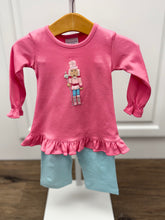 Load image into Gallery viewer, Dress your little one in festive charm with the Girls Applique Nutcracker Ruffle Pant Set by Squiggles. Crafted from soft 100% pima cotton, this set combines comfort with playful style. The bright pink tunic features a delicate pastel Nutcracker applique and a flirty ruffle hem, perfectly complemented by coordinating mint and white striped pants. 