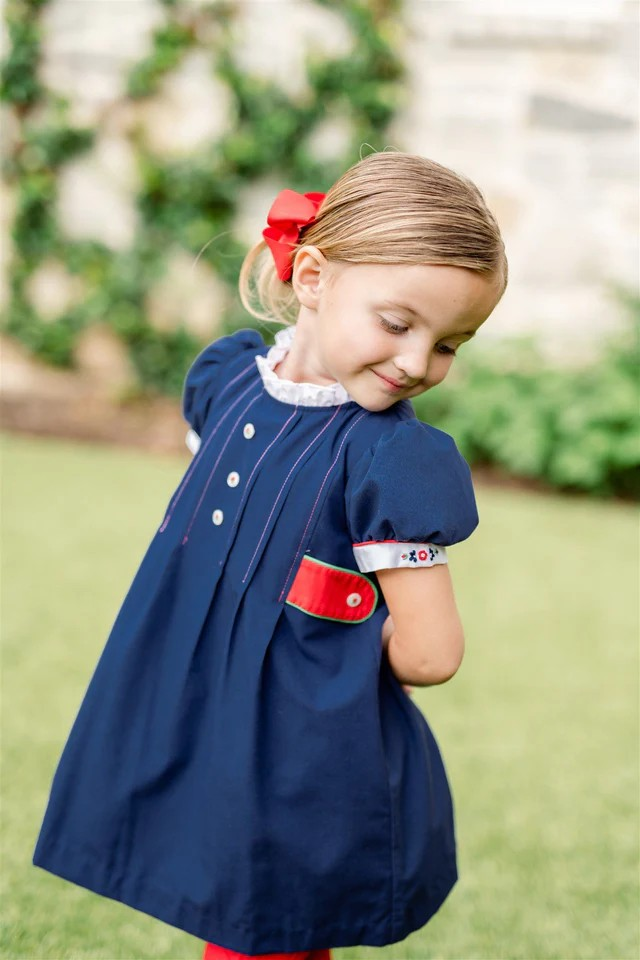Girls Gianna Navy Dress from The Proper Peony. Classic navy and red with pops of green, is always a proper selection and so picture perfect! Did you notice the green edging and red rosebud buttons down the front?