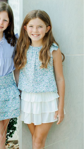 This girl's Allie Meadow Top from Pleat features a soft green and blue floral print, delicate ruffle shoulders, and cap sleeves for a charming and feminine look. The blousy feel adds comfort and ease, making it perfect for any occasion. Pair it with the coordinating tiered skirt for a complete and stylish outfit.