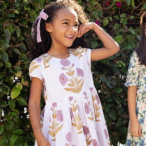 Peek A Boo! Oversized wild dandelions bloom against a 100% cotton vintage cotton voile on our extra special Girls Marisol Dress. Full of surprises, this short sleeve vintage-inspired piece has a purple lining peeking out from behind the scalloped hem and a set of sparkly glitter buttons at the back. 