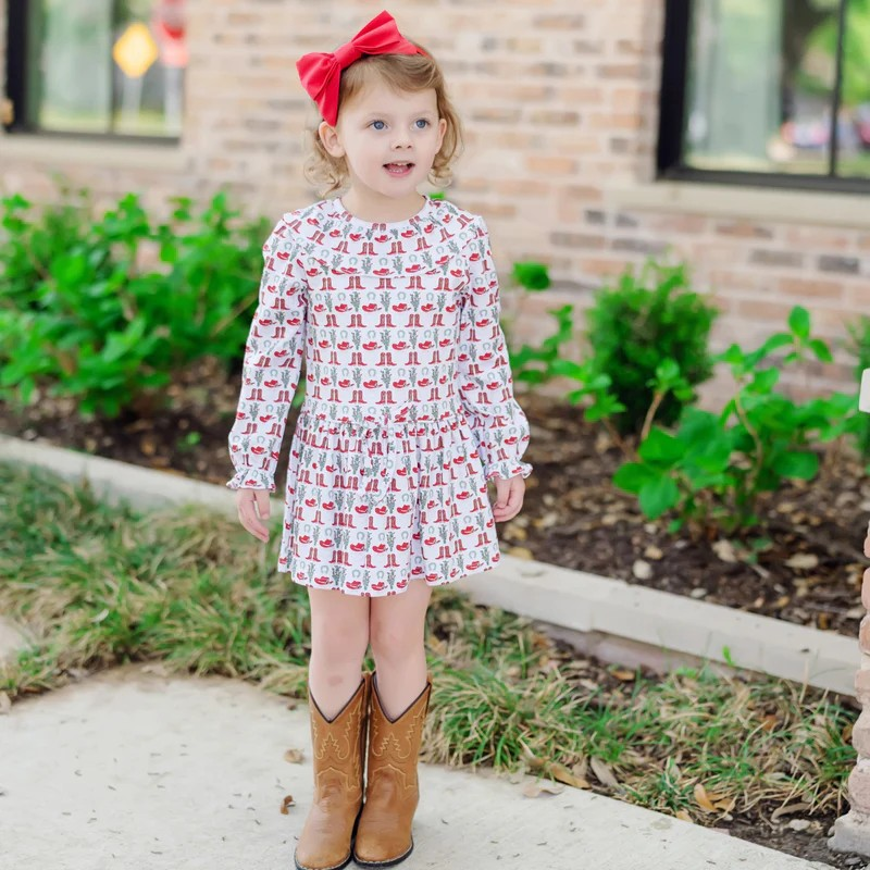 Dress your little one in festive charm with the Ellery Girls Dress in the Cowboy Christmas print by Lila & Hayes. Crafted from soft, breathable pima cotton knit, this long sleeve dress features a delicate ruffled yoke collar and a drop waist accented by a playful tie tassel. Elastic ruffled cuffs add a refined touch while ensuring comfort. Adorned with whimsical boots and Santa motifs, it’s the perfect holiday outfit for joyful celebrations and lasting memories.