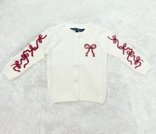 Elevate your little girl's wardrobe with our Girl's Red Bow Cardigan by Duffield Lane! This charming white knit cardigan features darling bows on both the sleeves and chest, adding a touch of sweetness to any outfit. Perfect for any occasion, this cardigan will keep her warm and stylish.