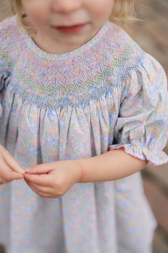 The Smocked Pumpkin Floral Analisa Bishop Dress from Shop Teeta combines charming fall florals with a delicate smocked neckline, creating an adorable look for infant girls. Its playful A-line silhouette allows for comfortable movement while showcasing a timeless design perfect for any autumn occasion. This piece offers both style and softness, making it a must-have for your little one’s wardrobe.