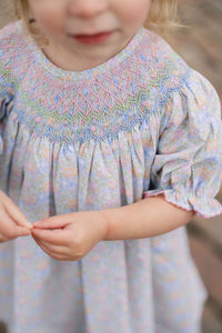 The Smocked Pumpkin Floral Analisa Bishop Dress from Shop Teeta combines charming fall florals with a delicate smocked neckline, creating an adorable look for infant girls. Its playful A-line silhouette allows for comfortable movement while showcasing a timeless design perfect for any autumn occasion. This piece offers both style and softness, making it a must-have for your little one’s wardrobe.