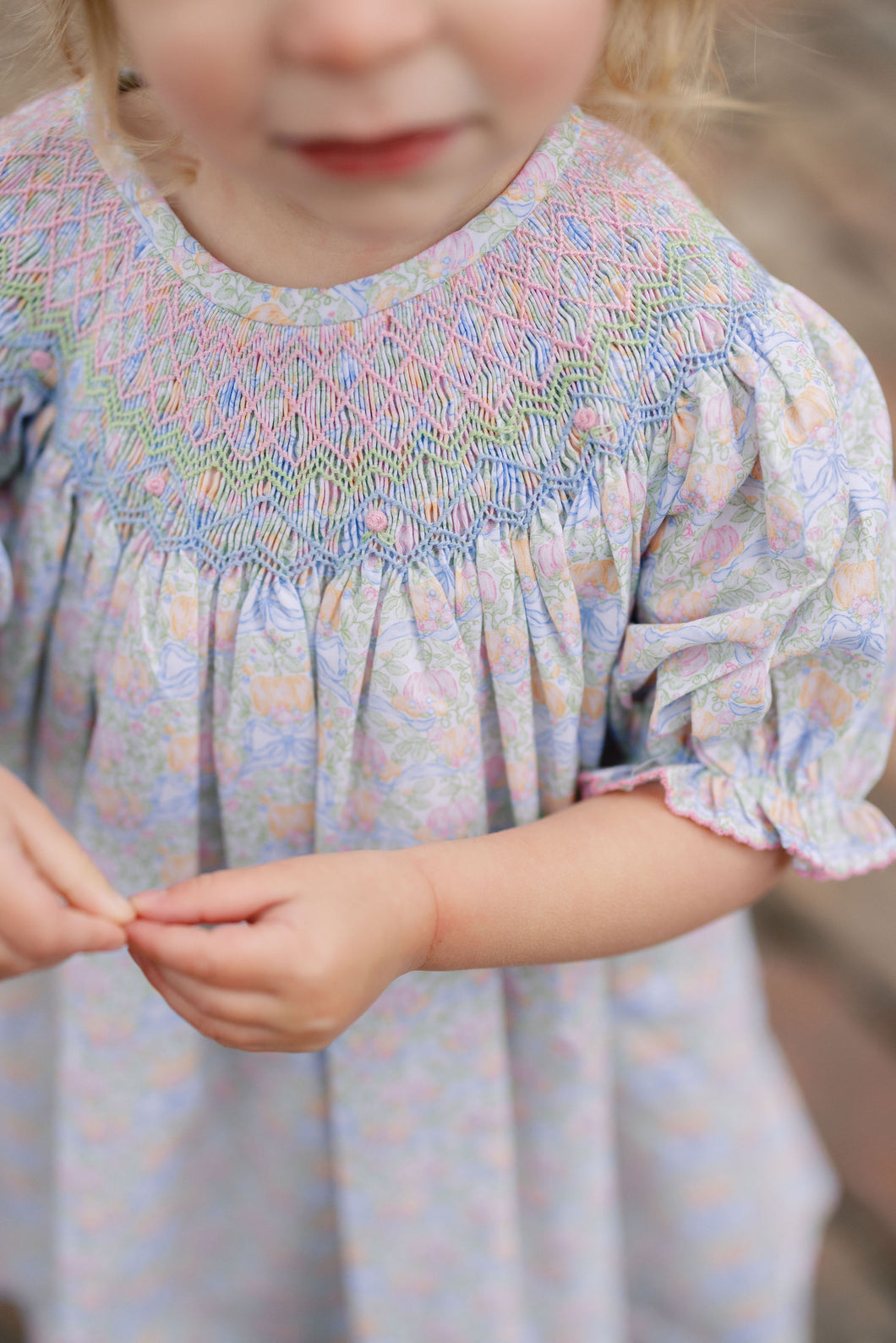 The Smocked Pumpkin Floral Analisa Bishop Dress from Shop Teeta combines charming fall florals with a delicate smocked neckline, creating an adorable look for infant girls. Its playful A-line silhouette allows for comfortable movement while showcasing a timeless design perfect for any autumn occasion. This piece offers both style and softness, making it a must-have for your little one’s wardrobe.
