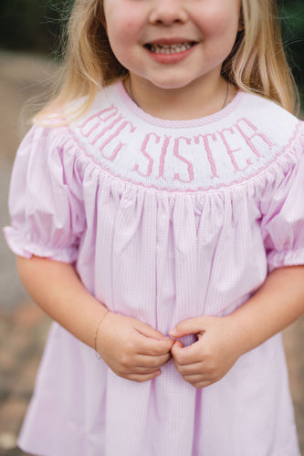 Celebrate her special role with the Girls Big Sister Bishop Dress from Shop Teeta. Featuring a charming pink and white gingham print and a delicate smocked neckline embroidered with 