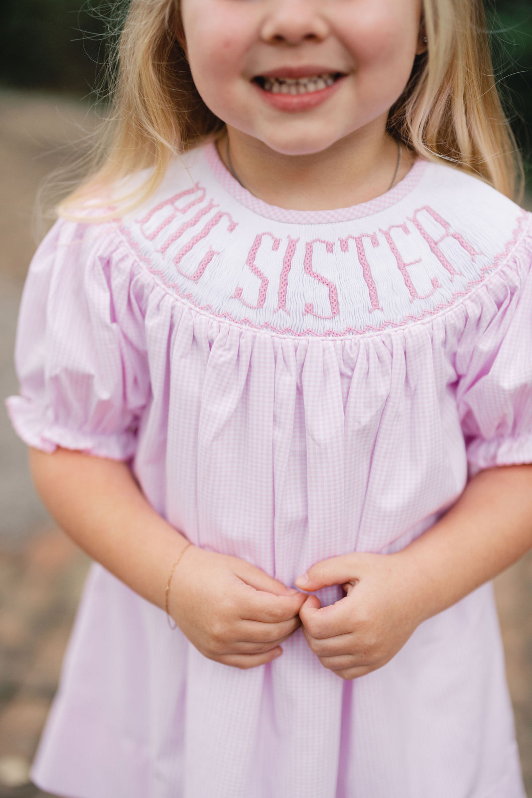 Celebrate her special role with the Girls Big Sister Bishop Dress from Shop Teeta. Featuring a charming pink and white gingham print and a delicate smocked neckline embroidered with 