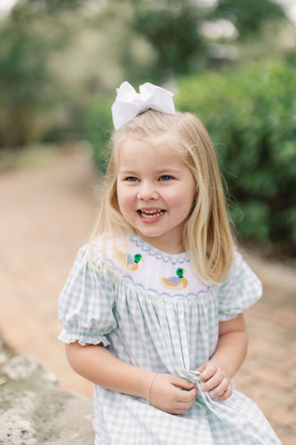 Dress your little one in timeless charm with the Smocked Bishop Kate Mallard Dress by Shop Teeta. Featuring a classic green and white gingham check, this dress is adorned with delicate smocking at the neckline and detailed embroidered mallard ducks, adding a sweet and playful touch. Perfect for coordinated family moments, it also pairs beautifully with matching sibling styles. This piece combines traditional design with exceptional craftsmanship, making it an irresistible choice for any special occasion or 