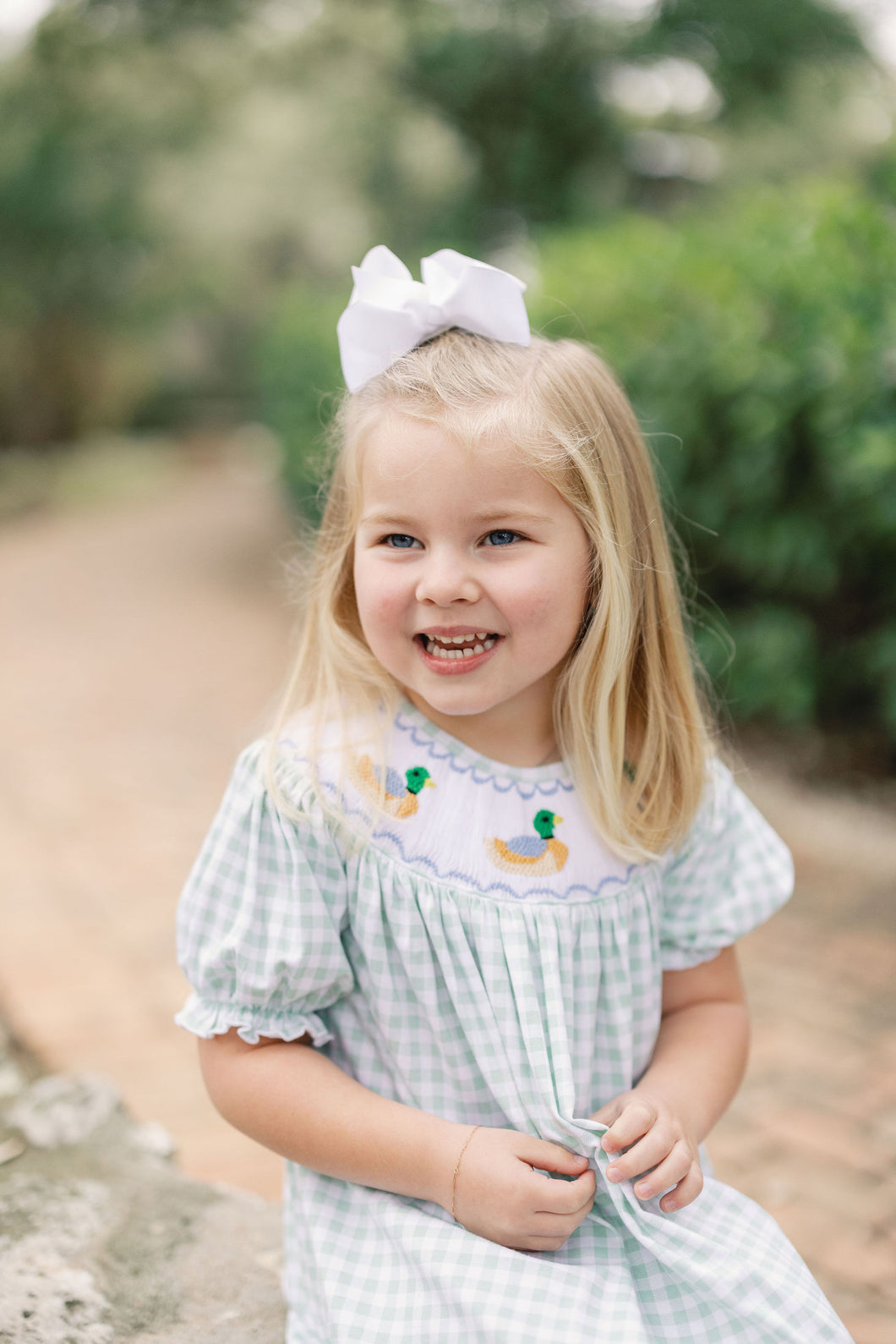Dress your little one in timeless charm with the Smocked Bishop Kate Mallard Dress by Shop Teeta. Featuring a classic green and white gingham check, this dress is adorned with delicate smocking at the neckline and detailed embroidered mallard ducks, adding a sweet and playful touch. Perfect for coordinated family moments, it also pairs beautifully with matching sibling styles. This piece combines traditional design with exceptional craftsmanship, making it an irresistible choice for any special occasion or 