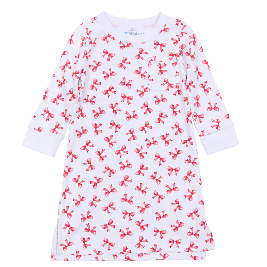 The Girls Scarlett Bows Long Sleeve Nightdress by Magnolia Baby offers cozy comfort with a charming holiday touch. Featuring a soft white fabric adorned with printed playful red bows, this knee-length nightgown keeps your little girl warm and stylish through every night. Its long sleeves provide extra warmth, making it perfect for festive celebrations or everyday bedtime. 