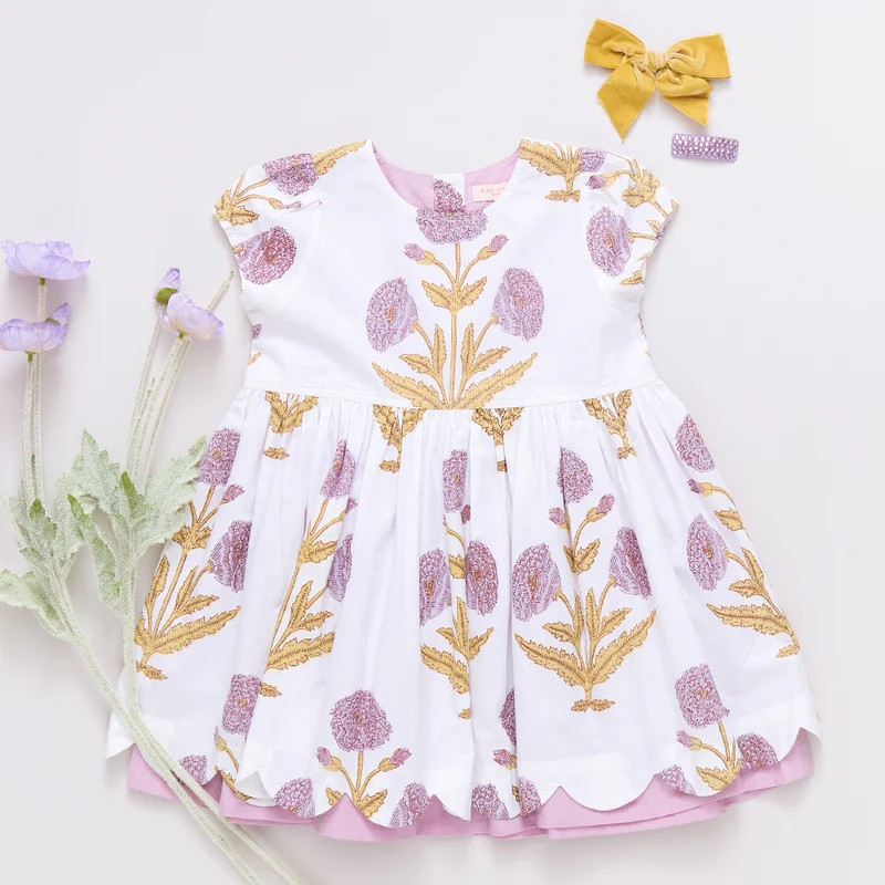 Peek A Boo! Oversized wild dandelions bloom against a 100% cotton vintage cotton voile on our extra special Girls Marisol Dress. Full of surprises, this short sleeve vintage-inspired piece has a purple lining peeking out from behind the scalloped hem and a set of sparkly glitter buttons at the back. 