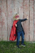 Load image into Gallery viewer, This adorable reversible cape offers twice the fun with quality design and versatility. The black satin side features a yellow bat emblem and reverses to a red spider web satin print on the reverse side with large black velour foam spider details. The Velcro closure at the neck makes switching superheroes a breeze.
