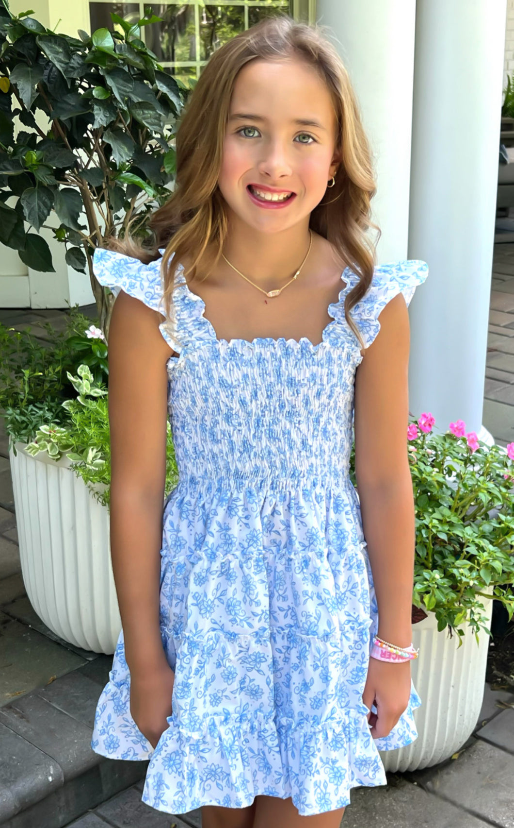 Experience the beauty of spring and summer in our Charlotte Blue Floral Dress from Be Elizabeth! Featuring a classic blue and white floral design, a tiered skirt for a flowy silhouette, a smocked bodice for a comfortable fit, and flutter sleeves for a touch of charm. Perfect for your stylish tween's wardrobe!