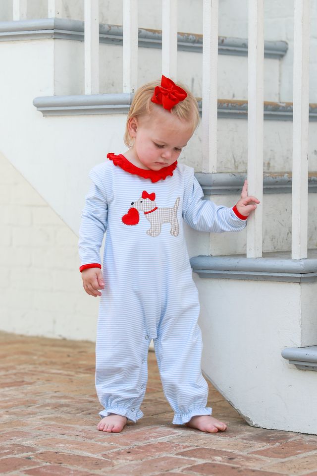 Introducing the Trotter Street Kids Infant Girls Puppy Love Ruffle Romper! This adorable romper is the perfect addition to your little one's wardrobe. Made with soft, light blue striped fabric and featuring cute red accents and an appliqué of a puppy holding a heart, your baby will be both comfortable and stylish.