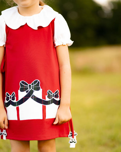 Girls Presents Emma Dress from The Yellow Lamb. Features a red jumper with applique plaid presents on each side. Fun & playful way to celebrate the holidays. Pair with a peter pan shirt and tights for a pulled together look. 