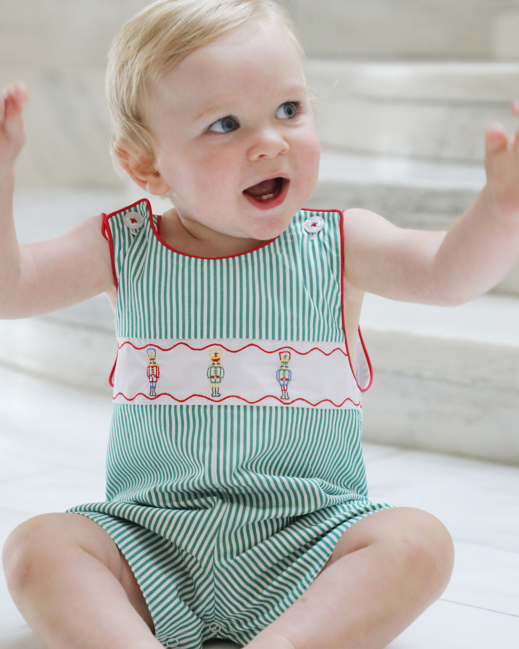 Dress your little one in festive charm with the Boys Jean Nutcracker Jon Jon from The Yellow Lamb. This adorable outfit features a classic green and white stripe pattern accented by detailed nutcracker embroidery on the front. Ideal for Santa visits or family photos, it combines comfort and holiday spirit effortlessly, making your baby the star of any seasonal occasion.