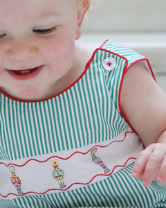 Dress your little one in festive charm with the Boys Jean Nutcracker Jon Jon from The Yellow Lamb. This adorable outfit features a classic green and white stripe pattern accented by detailed nutcracker embroidery on the front. Ideal for Santa visits or family photos, it combines comfort and holiday spirit effortlessly, making your baby the star of any seasonal occasion.