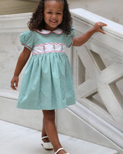 Load image into Gallery viewer, The Girls Nutcracker Kelly Dress from The Yellow Lamb combines festive charm with elegant details, featuring green and white stripes complemented by an embroidered sash adorned with Nutcracker motifs. Accented with refined piping along the Peter Pan collar and sleeves, this dress is a perfect choice for Christmas pictures and magical Santa visits, ensuring your little one looks both classic and captivating this holiday season.
