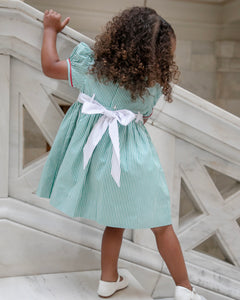 The Girls Nutcracker Kelly Dress from The Yellow Lamb combines festive charm with elegant details, featuring green and white stripes complemented by an embroidered sash adorned with Nutcracker motifs. Accented with refined piping along the Peter Pan collar and sleeves, this dress is a perfect choice for Christmas pictures and magical Santa visits, ensuring your little one looks both classic and captivating this holiday season.