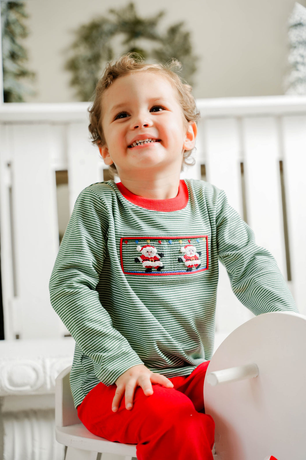 This charming green and white mini striped long sleeve tee features a smocked front adorned with delicate hand-embroidered Santas, adding a unique festive touch. Perfectly paired with the coordinating red cords, it creates a stylish holiday outfit your little one will love. Sibling matching options make family photos even more memorable. Celebrate the season with comfort and timeless style in this playful Santa Claus tee.