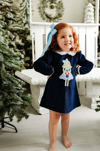 Dress your little one in festive charm with the Girls Navy Nutcracker Louisa Dress from Zuccini Kids. This long-sleeve, navy knee-length dress features a delicate ruffled Peter Pan collar and a stunning nutcracker applique that brings holiday magic to life. Crafted for comfort and style, it’s perfect for special occasions, making your child feel both elegant and joyful. Matching sibling looks available.
