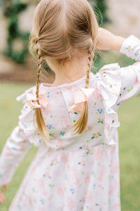 The Girls En Pointe Twirl Dress from The Proper Peony features a soft knit fabric adorned with an elegant ballet and bow print. Its charming ruffle detail and flowy design invite endless twirling, making it perfect for a day filled with dance and delight. Comfortable and stylish, this dress is sure to inspire her graceful moves and joyful moments.