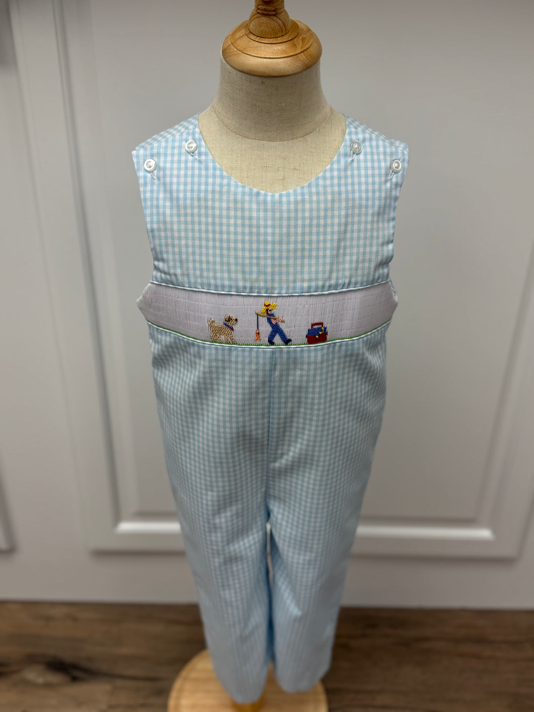 This Boys Gone Fishing Longall showcases a charming blue and white gingham pattern, highlighted by a detailed smocked fisherman & his best friend embroidery on the front. Designed for comfort and style, it pairs perfectly with a classic Peter Pan collar shirt, creating an adorable and polished outfit ideal for playful days and special occasions.