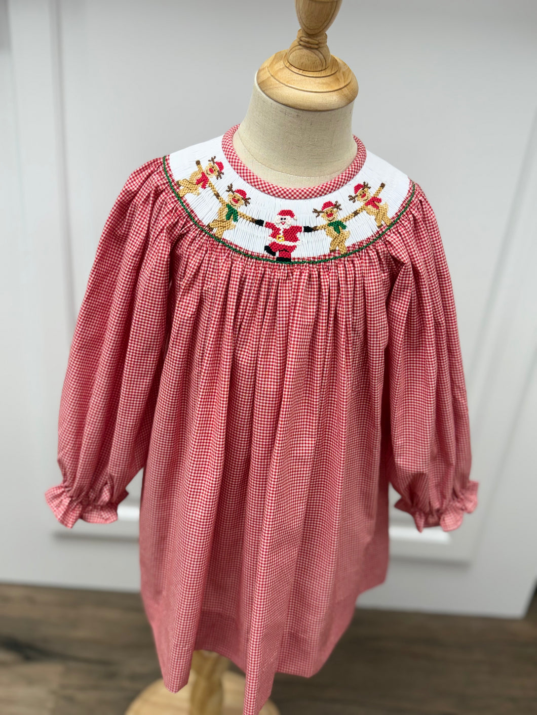 Dress your little one in festive charm with the Girls Rockin' Reindeer Bishop Dress from Cape Point Clothing Co. This vibrant red and white gingham dress features a smocked neckline adorned with playful dancing reindeer and Santa motifs, perfectly capturing holiday joy. The dress style offers a comfortable yet stylish fit, making it ideal for holiday gatherings or special occasions. Celebrate the season in a look that’s both adorable and timeless.