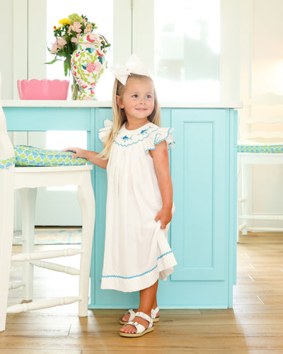 Elevate your little one's beach style with our White Marlin Smocked Bishop Dress. Made from crisp white pique fabric, this dress features a smocked neckline, flutter sleeves, and vibrant blue marlin embroidery. Perfect for any beach day, it's a must-have for your toddler's wardrobe!