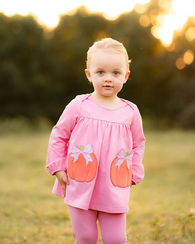 Dress your little one in festive charm with the Pumpkins Tabby Tunic and Legging Set from The Yellow Lamb. This bright pink outfit features playful pumpkin appliques as pockets and delicate bow accents, perfect for celebrating fall and Halloween in style. Comfortable and cute, it’s ideal for keeping her cozy and picture-ready at every seasonal event.