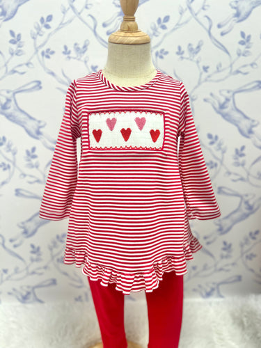 Dress your little one in style with the Girls Valentine Hearts Smocked Pant Set by Anavini! This set features a red and white striped tunic shirt with ruffled trim and a charming pink and red heart smocking design. Complete the look with the adorable red pants. Perfect for Valentine's Day or any occasion, this set will make your little girl look and feel extra special!