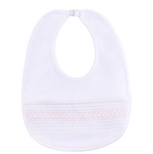 Load image into Gallery viewer, The Baby Smocked Bullion Bib by Feltman Brothers is a timeless accessory for your little one! This adorable baby bib matches perfectly with our Infant Smocked Bullion Gown and Hat and would be a perfect gift set! Perfect as a baby gift for your loved one, or as an heirloom piece to treasure forever! 

We carry the White/Blue and the White/Pink. The double pink bib in the lifestyle picture is not a color we carry, just a glimpse of this precious piece! 
