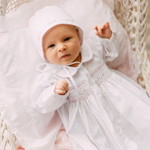 Load image into Gallery viewer, Feltman Brothers’ Girls Smocked Bud Take Me Home Gown wraps your little one in timeless elegance. The delicate pink smocking and embroidered Peter Pan collar create a precious, classic look, while the matching bonnet adds a soft, charming finishing touch for unforgettable first moments.
