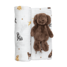 Load image into Gallery viewer, Mud Pie’s Lab Swaddle and Rattle Set is a delightful 2-piece collection designed to provide comfort and joy for your little one. The muslin swaddle blanket, measuring 47" x 47", is crafted from 100% cotton, ensuring a soft and breathable wrap for your baby. It comes beautifully rolled with a coordinating faux fur plush rattle, shaped like an adorable dog, measuring 8" in size. This charming set is perfect for snuggling, soothing, and playtime, making it an ideal gift for new parents!

