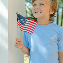 Load image into Gallery viewer, The J Bailey Boys Retriever on Heathered Blue Tee combines Southern charm with everyday comfort. This soft cotton-blend tee features a cheerful retriever clutching the US flag, perfect for young dog lovers and outdoor enthusiasts. Ideal for weekend adventures, casual play, and warm-weather style.
