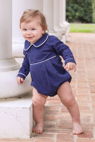 Dress your little one in timeless charm with the Joseph Bubble in Navy from Trotter Street. This classic navy bubble features a delicate Peter Pan collar and crisp white piping, adding a touch of elegance to your infant boy’s wardrobe. Personalize it with a name or monogram to create a cherished heirloom that will be treasured for years to come. Perfect for special occasions or everyday wear, this piece combines style and sentiment beautifully.