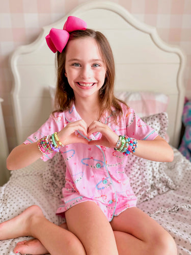 Get ready for stylish comfort with our Friendship Bracelet Pima Button Up Lounge Set! Designed for girls, this set includes a hot pink knit lounge shirt and matching shorts featuring every girl's favorite friendship bracelet design. Perfect for lounging or playing, from James & Lottie.