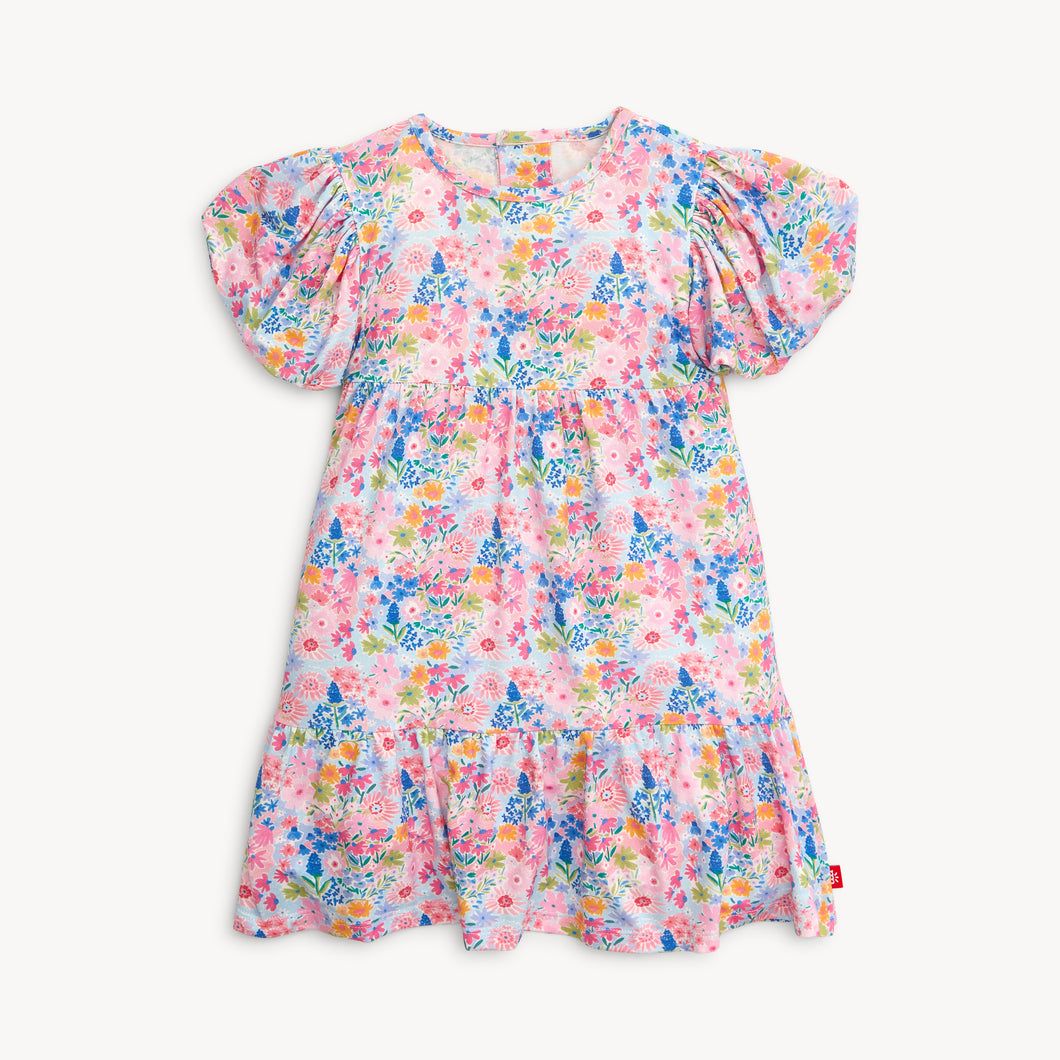 Experience the beauty of spring in our Lily Vibrant Floral Dress from Magnetic Me. Featuring a stunning floral pattern, cute puffy sleeves, and a charming tiered skirt, this dress is perfect for your little one. Plus, smaller sizes come with a convenient diaper cover.