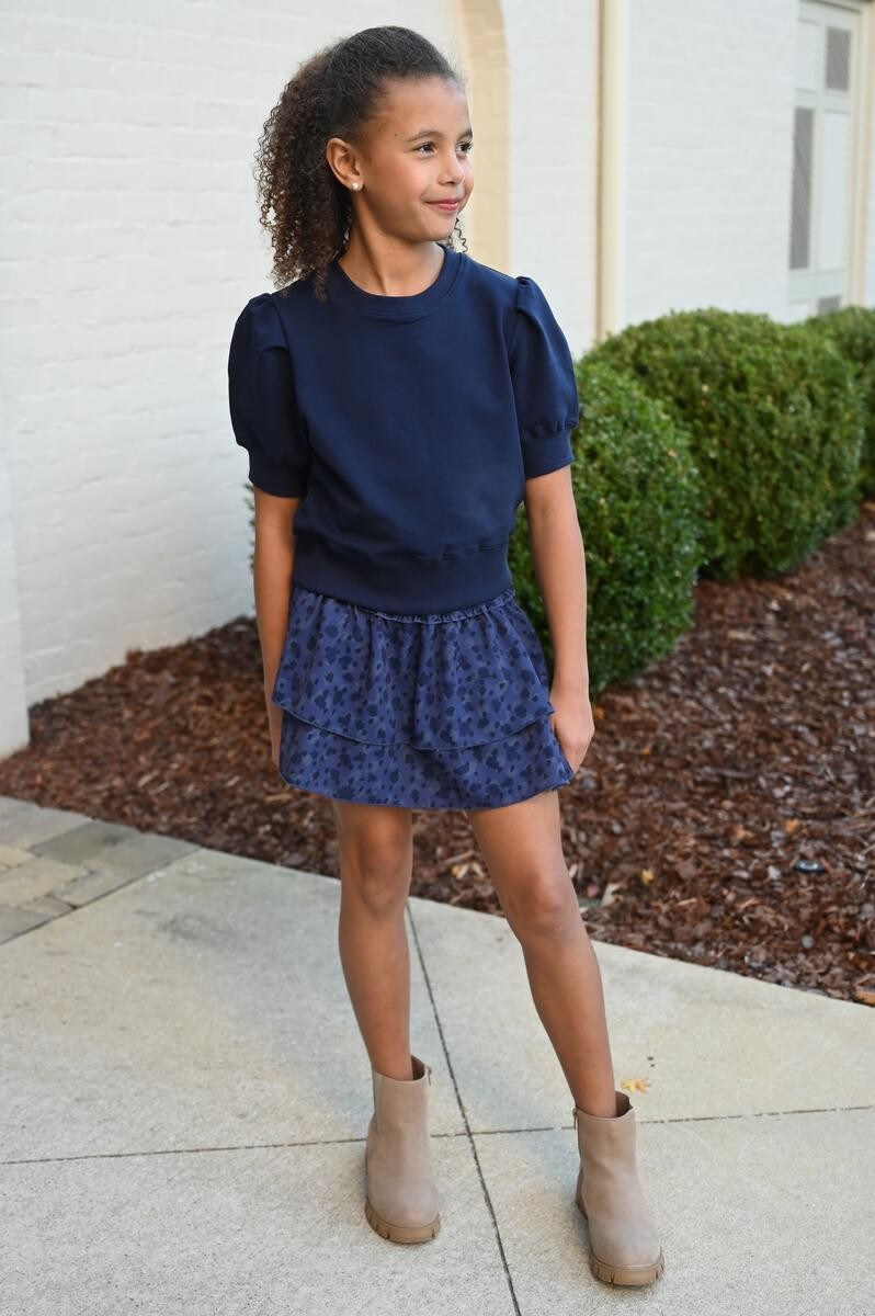 Elevate any outfit with our Riley Sweatshirt in Navy. This short sleeve, ruffle shoulder sweatshirt for tween girls is perfect for pairing with jeans or a skirt. Complete the look with our Scottie Spots Skirt from pleat.