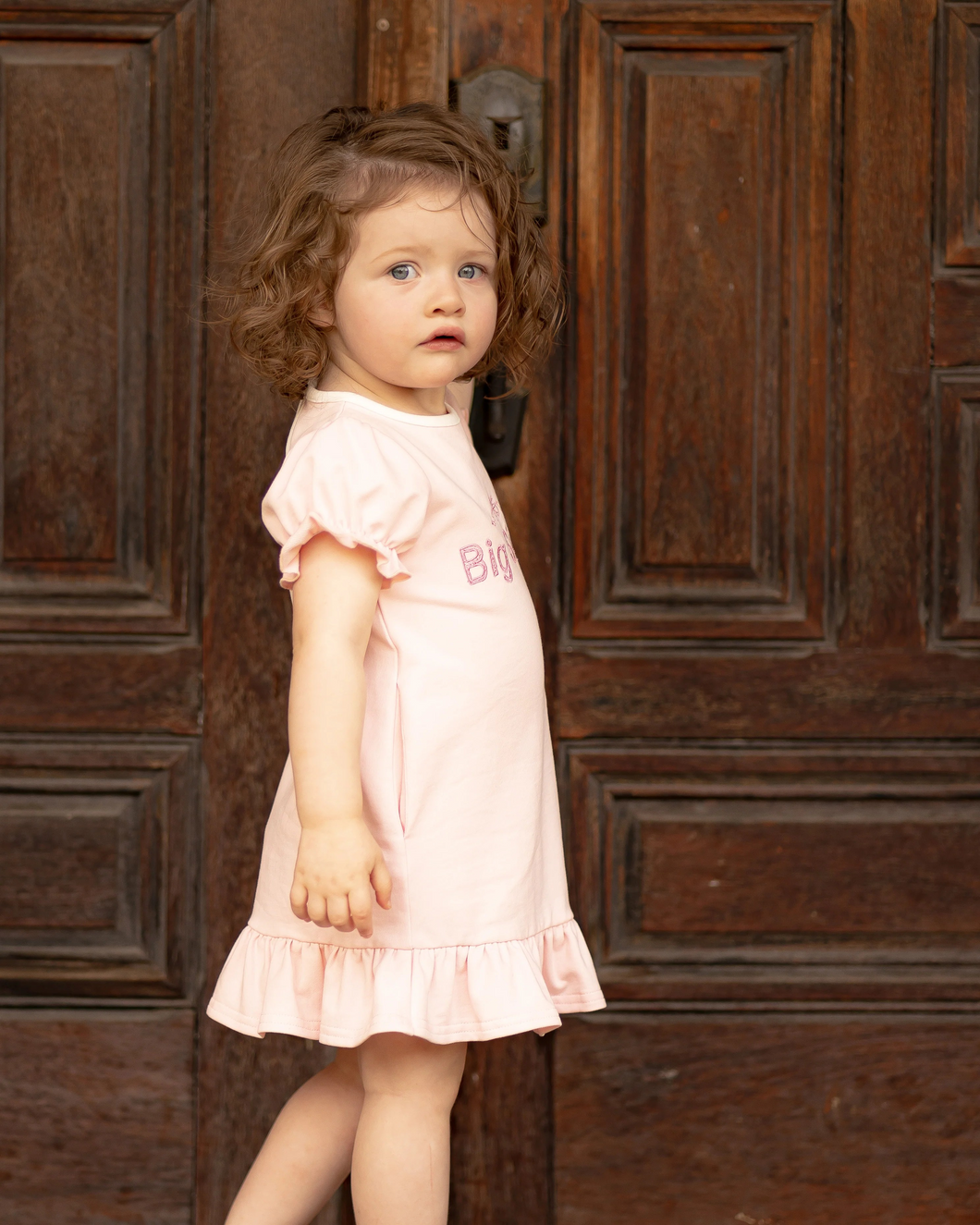 A sweet dress for the most precious Big Sister announcement! Ultra comfortable knit fabric with princess sleeves with elastic cuffs, crew neck with single button back closure. Fun ruffled dress hem. Custom bow and big sister embroidery on chest. Polyester spandex blend knit.