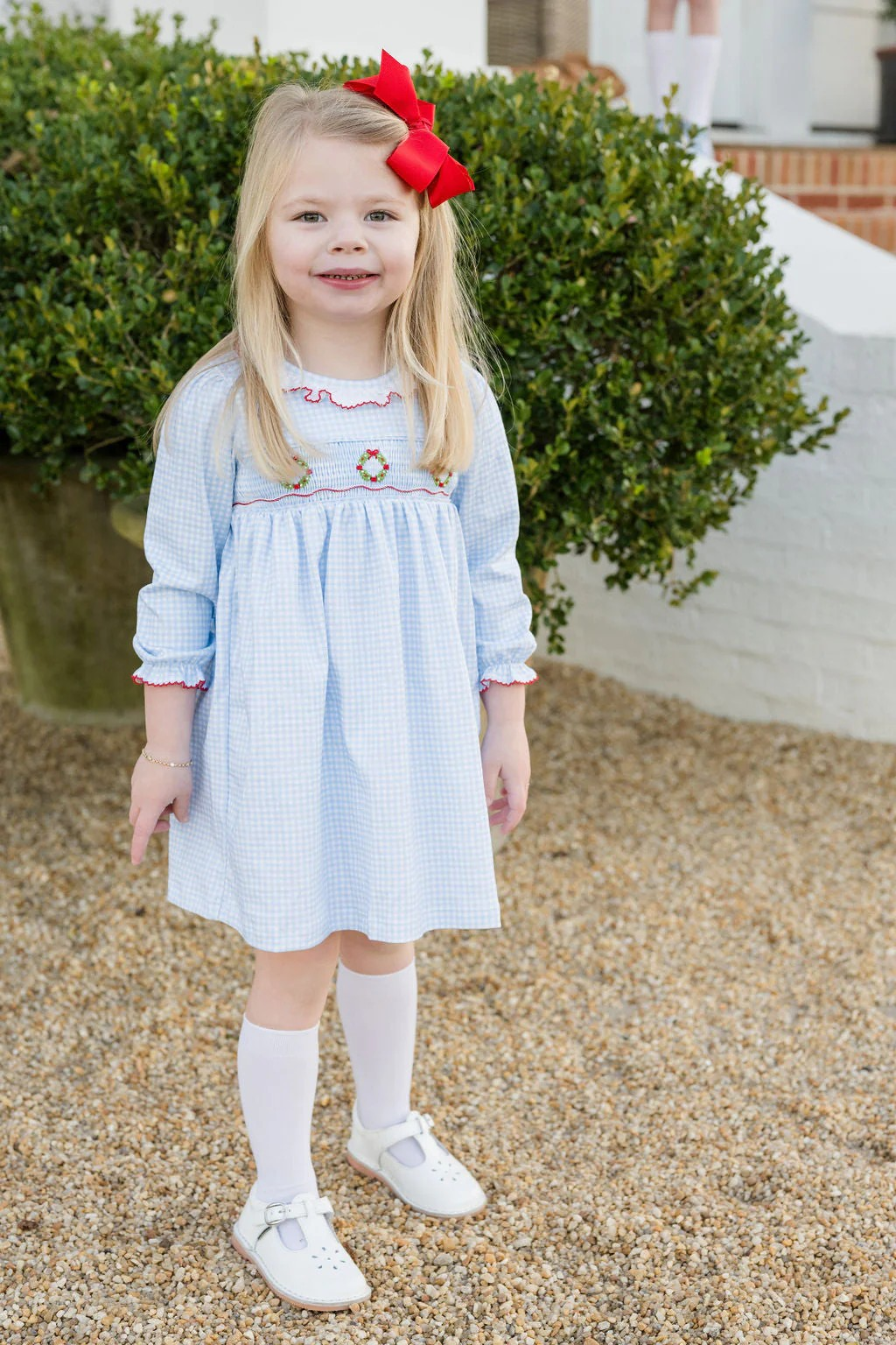 *Pre-Order

Girls Sara Smocked Wreath Long Sleeve Dress from James & Lottie brings festive charm to your little one's wardrobe. This delightful dress features a soft blue and white gingham knit with hand-smocked Christmas wreaths adorning the front, finished with an elegant ruffle-trimmed collar. Perfect for holiday celebrations and special occasions this season! Coordinate with the matching infant girls bubble to create adorable sibling sets that capture those precious moments together.