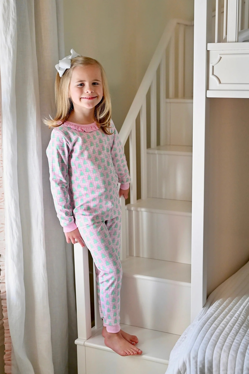 Cozy Christmas mornings just got cuter! These Girls 2-Piece Pink Gingham Christmas Tree Lounge Set from James & Lottie feature soft cotton footies in cheerful pink and white gingham with festive bright green trees scattered throughout. Ruffle neckline in pink and matching cuffs add adorable details. Perfect for holiday photos, family gatherings, or simply spreading seasonal cheer at home. Give your little one the comfort and style they'll love wearing all season long.