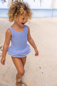 Bring the charm of Paris to the beach with this adorable skirted swimsuit. The blue and white seersucker stripes and white mini pompom accents give it a stylish and playful look. The airy open back with a bow detail adds a cute flair. Perfect for any fashionable toddler girl! From SnapperRock.