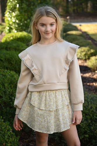 The Livvy Sweatshirt in Beige from Pleat adds a touch of elegance to your child's fall wardrobe with its charming ruffle details on each side. Perfectly paired with tiered skirts, it creates a polished look ideal for any autumn event or picture day. Comfortable yet stylish, this sweatshirt ensures your little one stands out with effortless grace.