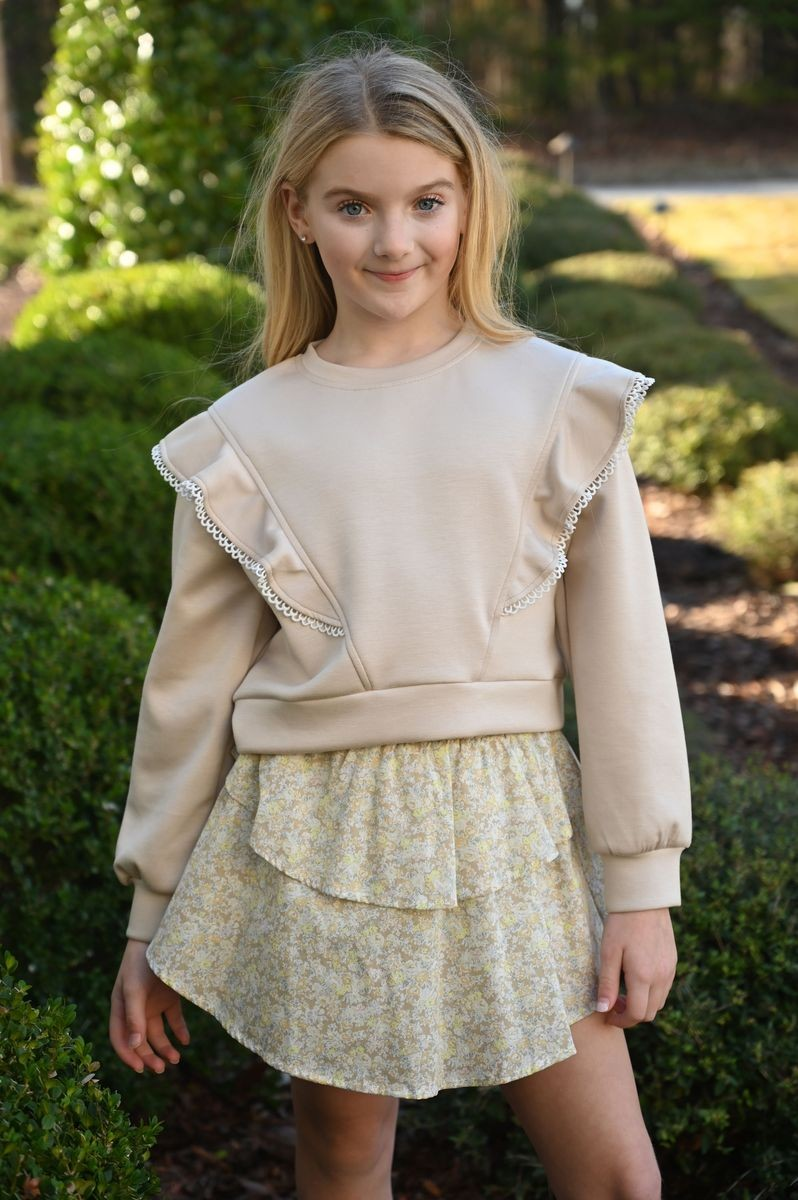 The Livvy Sweatshirt in Beige from Pleat adds a touch of elegance to your child's fall wardrobe with its charming ruffle details on each side. Perfectly paired with tiered skirts, it creates a polished look ideal for any autumn event or picture day. Comfortable yet stylish, this sweatshirt ensures your little one stands out with effortless grace.
