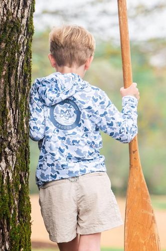 Boy's Pro Performance Hoodie Blue Camo is a long-sleeve, hooded performance fishing hoodie featuring a full camouflage pattern in cool coastal tones. Shades of steel blue, light gray, navy, and ice blue. Fabric is a lightweight, moisture-wicking synthetic blend designed for sun protection and breathability. Shirts have a relaxed fit with a straight hem and long sleeves, suitable for layering or wearing alone in warm conditions. 