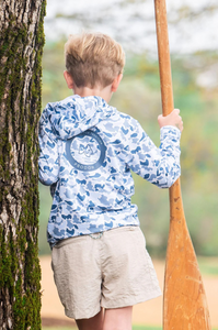 Boy's Pro Performance Hoodie Blue Camo is a long-sleeve, hooded performance fishing hoodie featuring a full camouflage pattern in cool coastal tones. Shades of steel blue, light gray, navy, and ice blue. Fabric is a lightweight, moisture-wicking synthetic blend designed for sun protection and breathability. Shirts have a relaxed fit with a straight hem and long sleeves, suitable for layering or wearing alone in warm conditions.&nbsp;